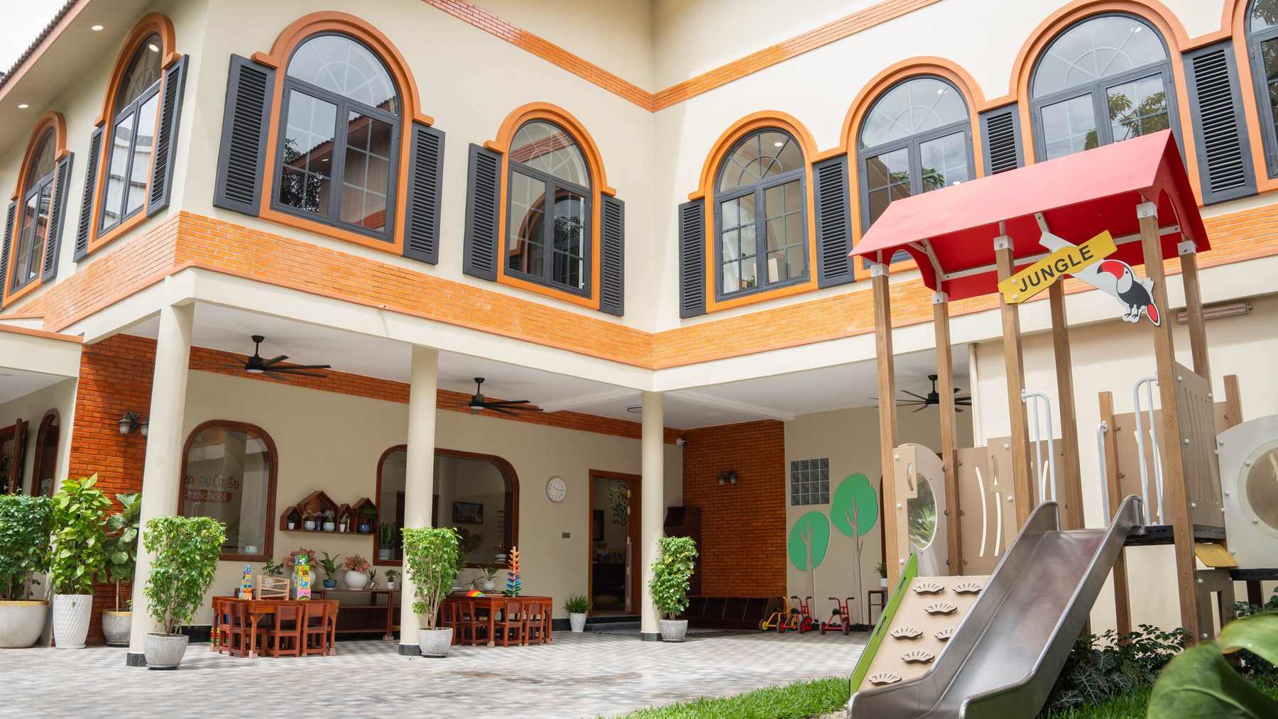 The Orange Crest Preschool courtyard after renovation, with the playhouse and slide below two storeys of arched windows