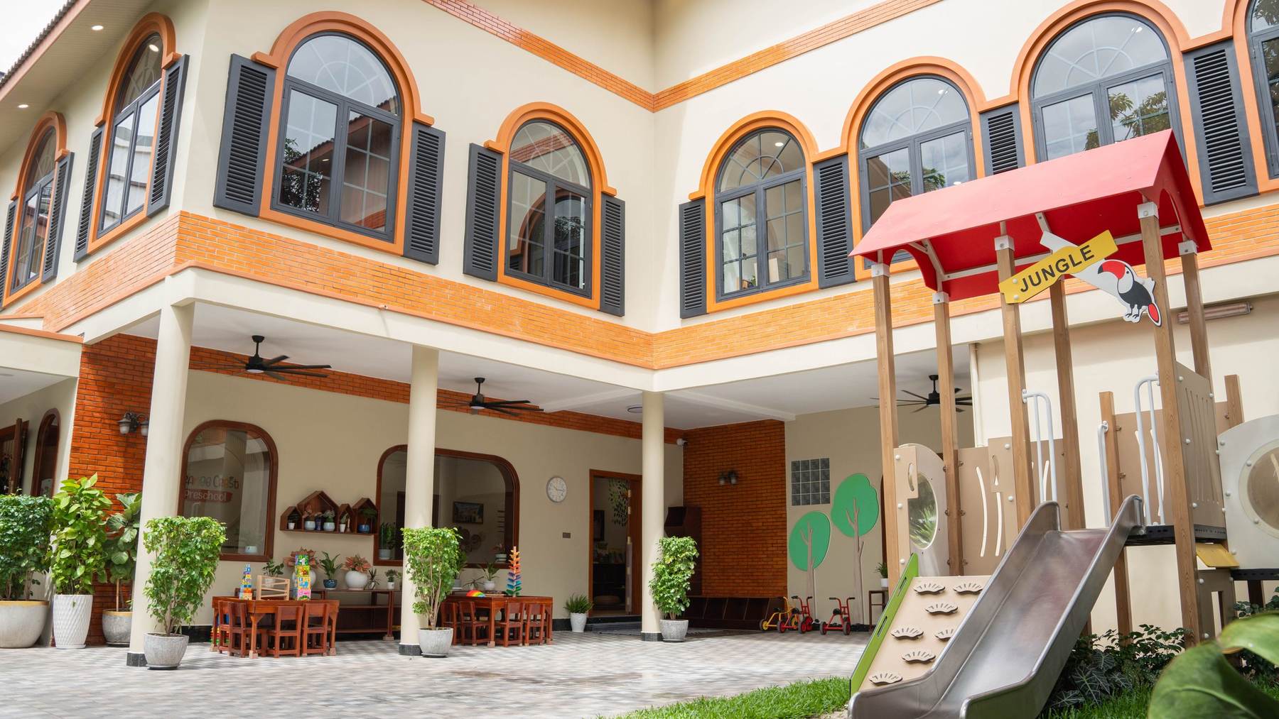 The Orange Crest Preschool courtyard after renovation, with the playhouse and slide below two storeys of arched windows