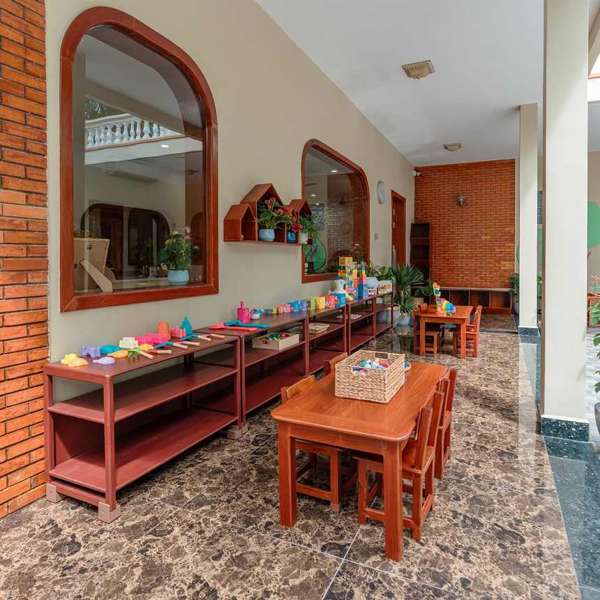 The covered brick arcade at Orange Crest Preschool, with low wooden tables set out along it