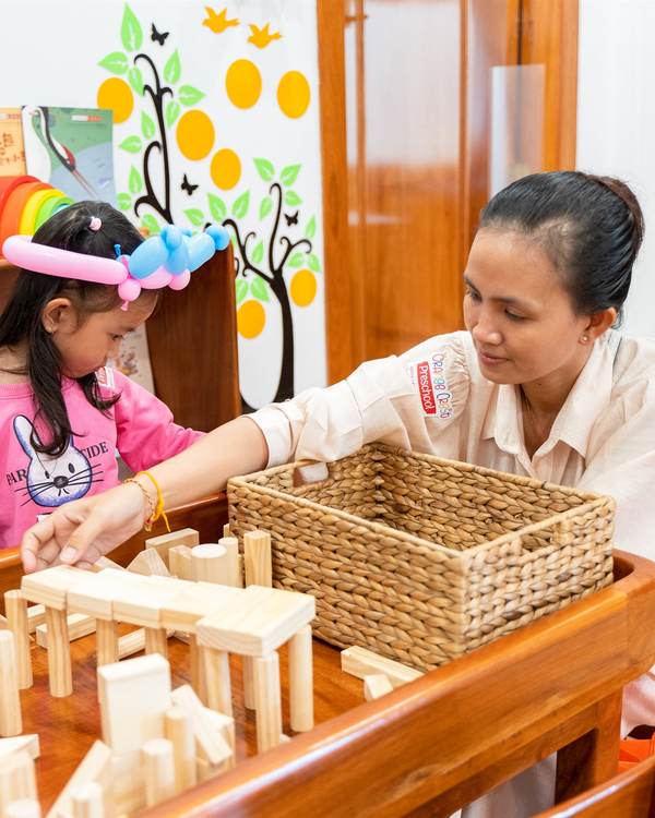 A teacher kneeling beside a child who is building with natural wooden blocks